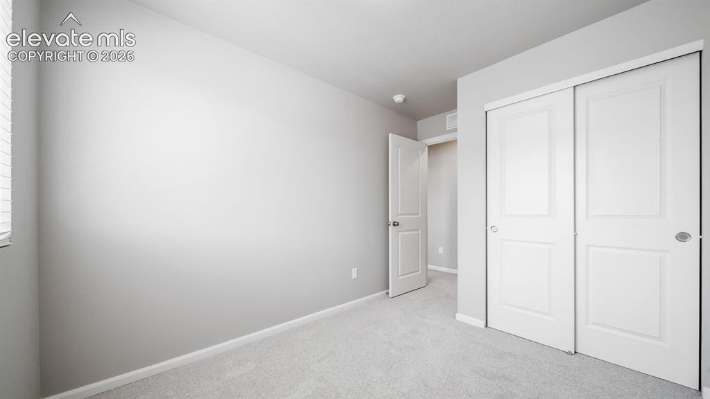 Image 10 of 28: Interior room with light gray walls, light carpet, and white baseboards