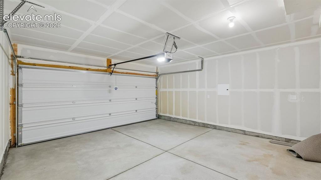 Image 24 of 28: Spacious garage featuring a concrete floor, overhead lighting, and a white