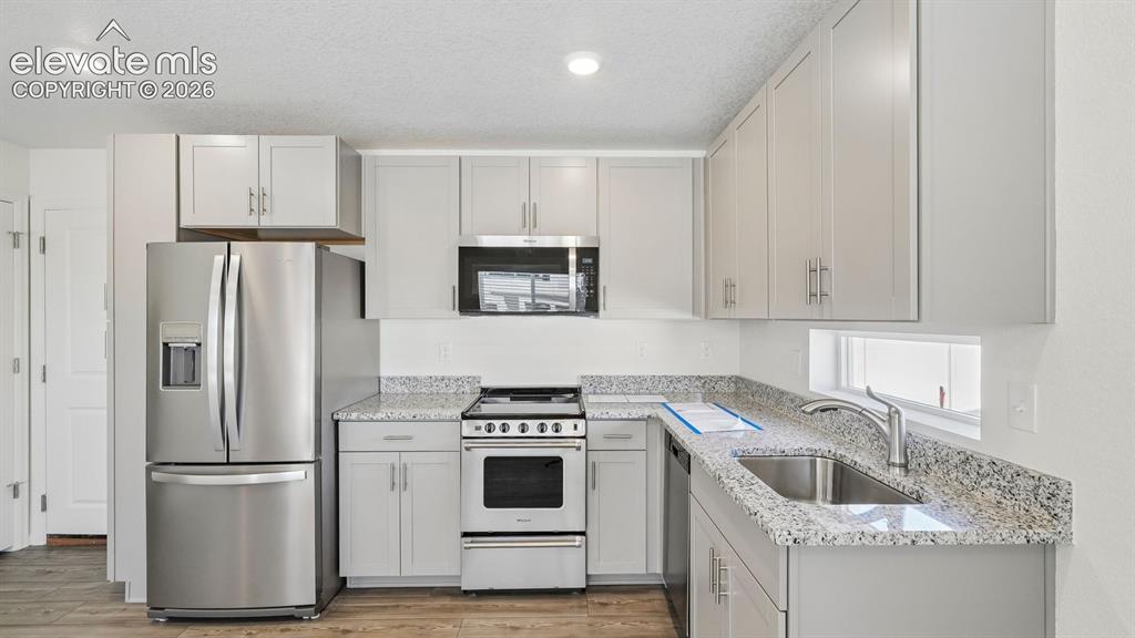Image 8 of 28: Kitchen featuring stainless steel appliances, light gray cabinetry, granite