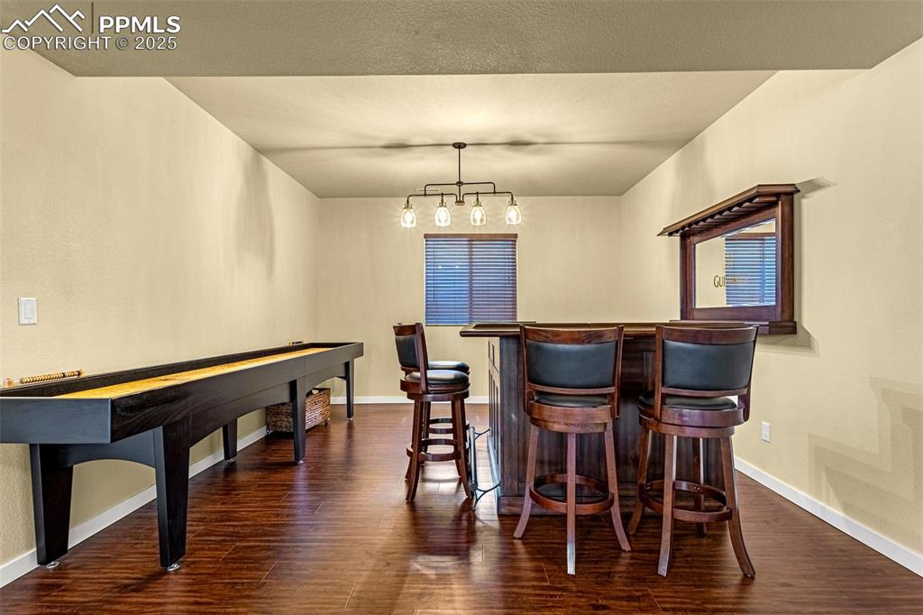 Image 21 of 42: Bar with hanging light fixtures, dark wood-type flooring, and an inviting c