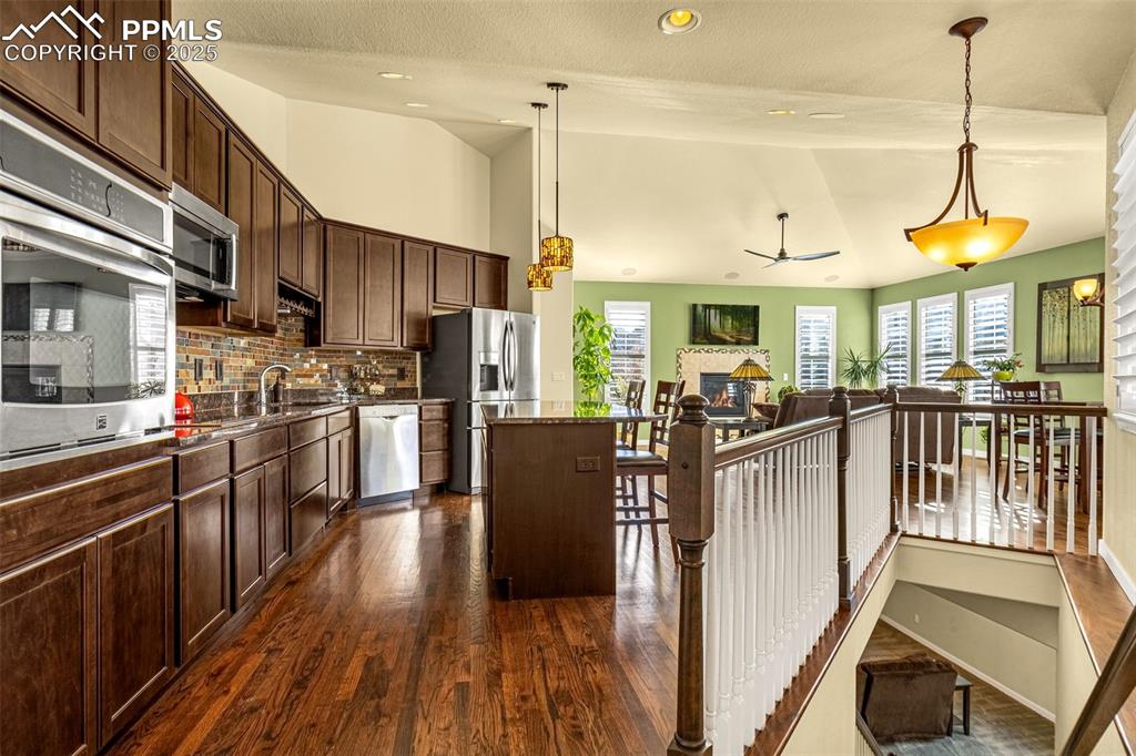 Image 4 of 42: Kitchen with lofted ceiling, dark brown cabinetry, hanging light fixtures,