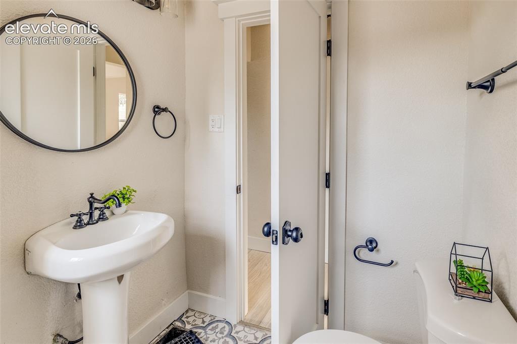 Image 18 of 27: Bathroom featuring a pedestal sink, round mirror with a black frame, patter