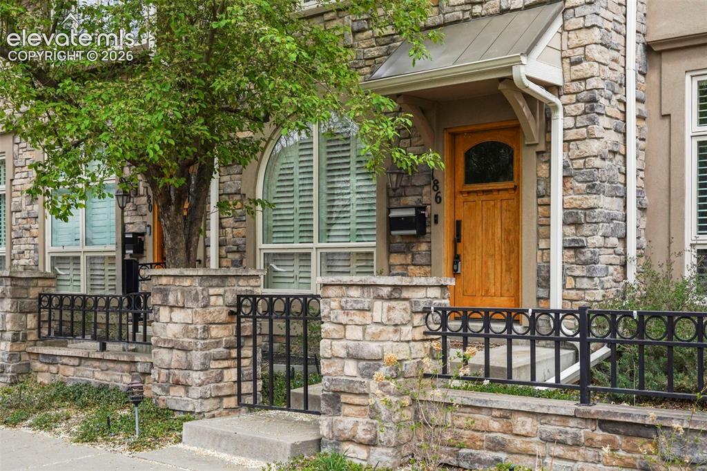 Image 2 of 34: Stone facade entry featuring a natural wood front door, decorative metal ra