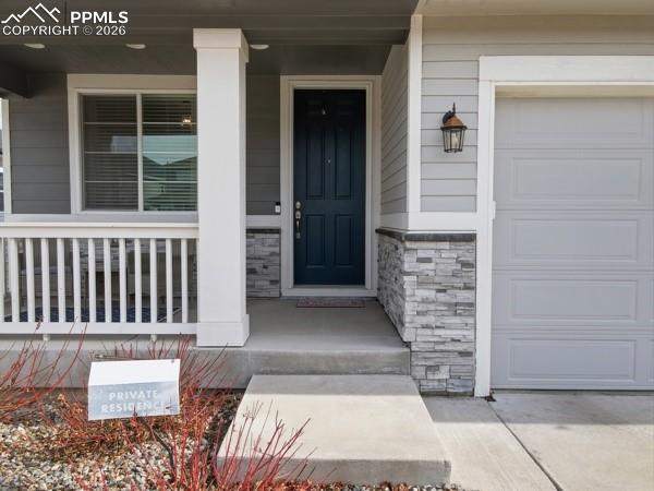 Image 27 of 36: Property entrance featuring a porch, stone siding, and a garage