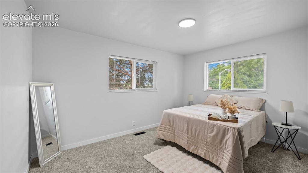 Image 11 of 21: Bedroom featuring two windows, light gray walls, and gray carpeting