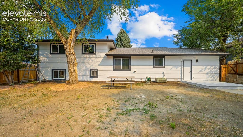 Image 20 of 21: White exterior with dark trim windows, mature trees, a concrete patio, and 