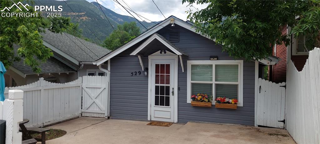 Caption: View of front of house with a mountain view, a shingled roof, a gate, and a patio area