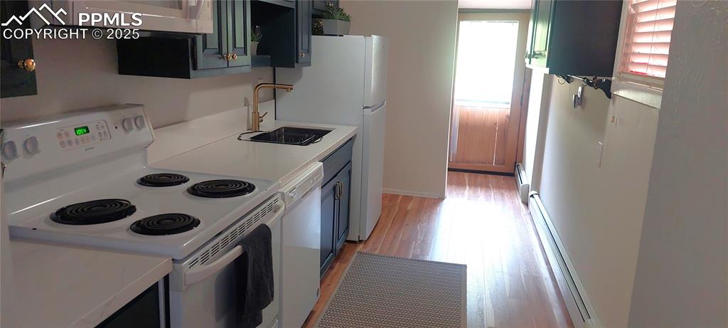 Image 18 of 46: Kitchen featuring white appliances, a baseboard heating unit, light wood-st