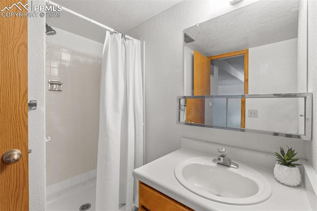 Image 20 of 29: Full bathroom featuring vanity, a shower stall, a textured wall, and a text