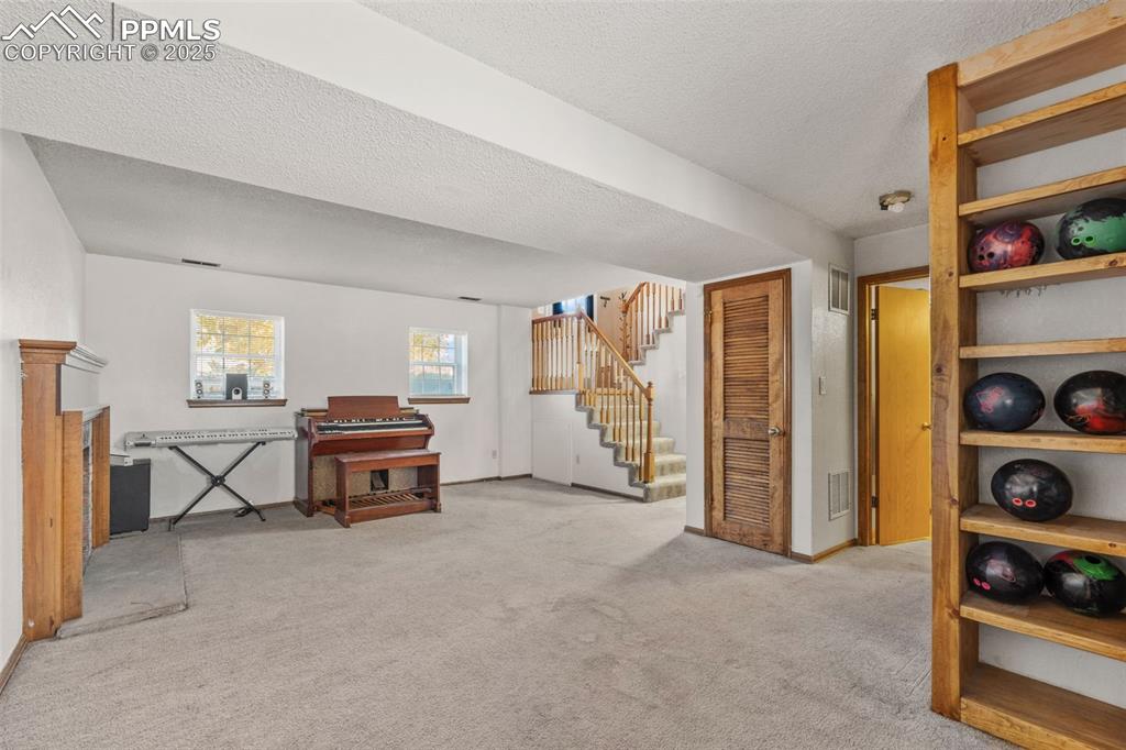 Image 24 of 29: Below grade area with light carpet, a textured ceiling, and stairs