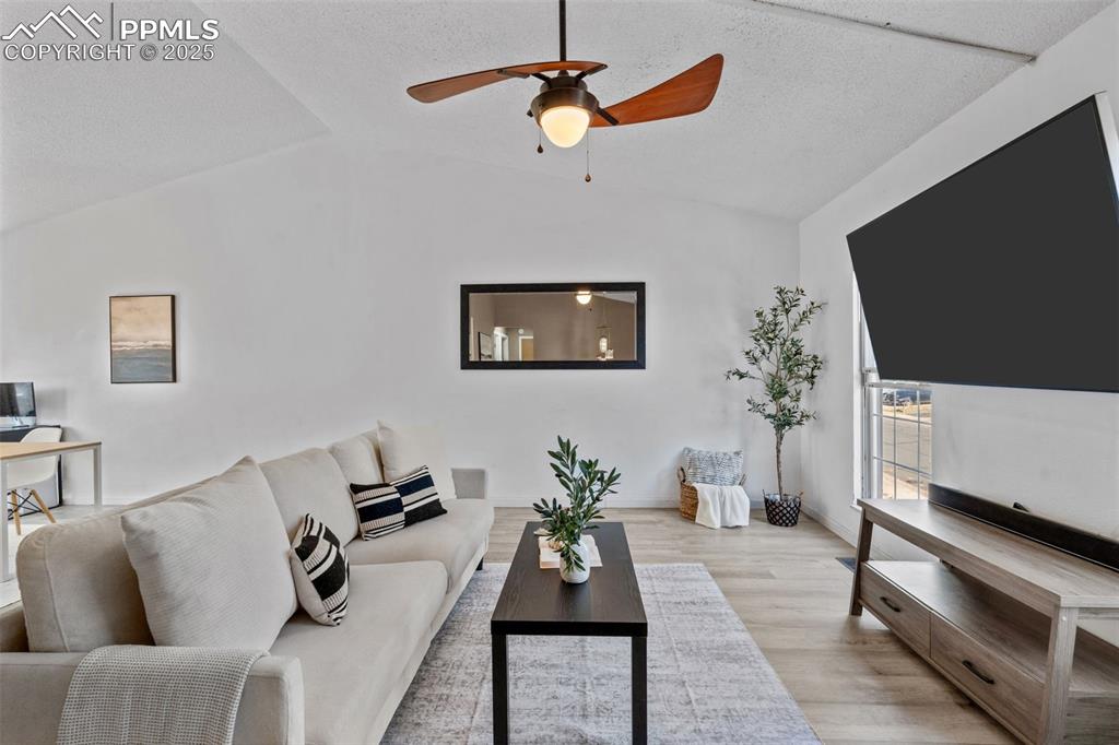 Image 8 of 29: Living area with wood finished floors, vaulted ceiling, a ceiling fan, and