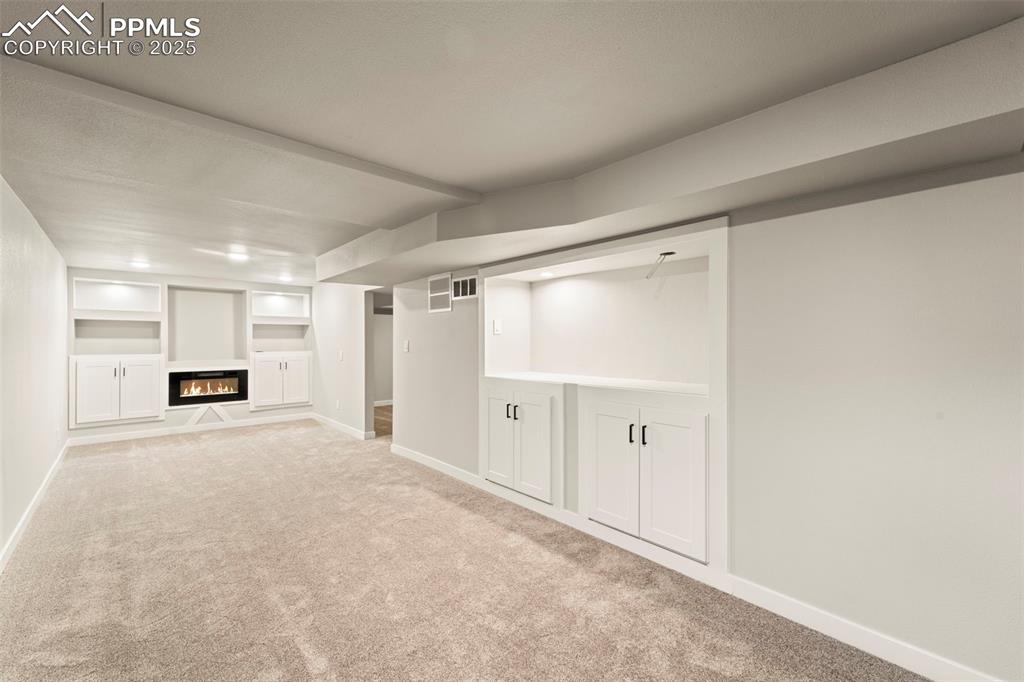Image 28 of 31: Finished basement with carpet floors, baseboards, built in shelves, and a g