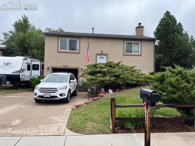Caption: Bi-level home with stucco siding, driveway, a garage, a front yard, and a chimney