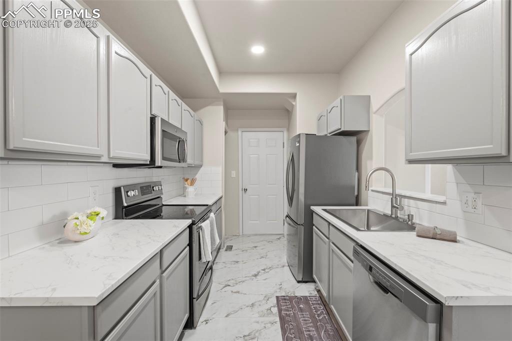 Image 13 of 42: Kitchen with backsplash, appliances with stainless steel finishes, gray cab
