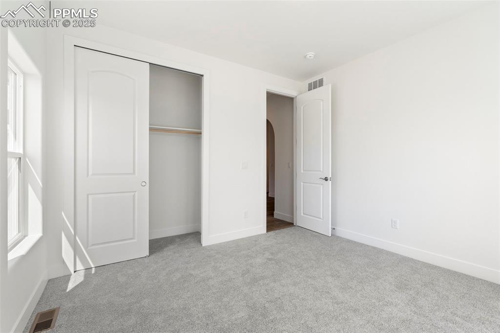 Image 31 of 34: Unfurnished bedroom with arched walkways, light carpet, and a closet