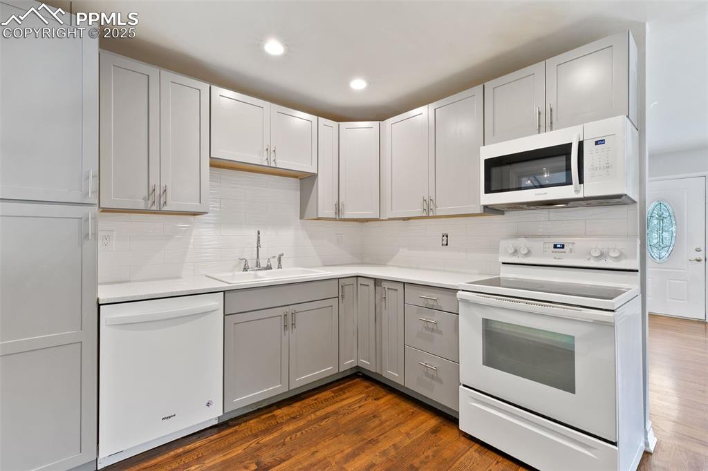 Image 6 of 36: Kitchen with white appliances, gray cabinets, tasteful backsplash, light co