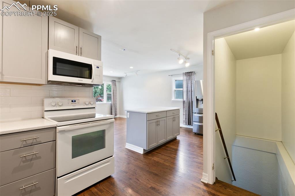 Image 8 of 36: Kitchen with gray cabinets, white appliances, rail lighting, dark wood-styl