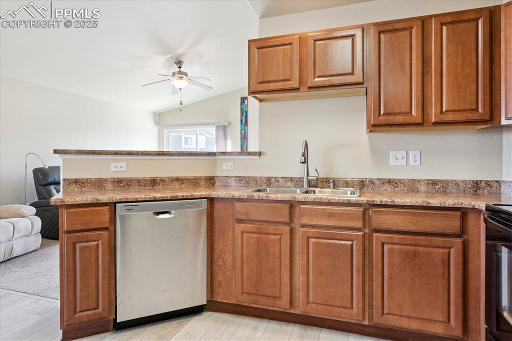 Image 4 of 29: Kitchen with brown cabinets, stainless steel dishwasher, vaulted ceiling, c