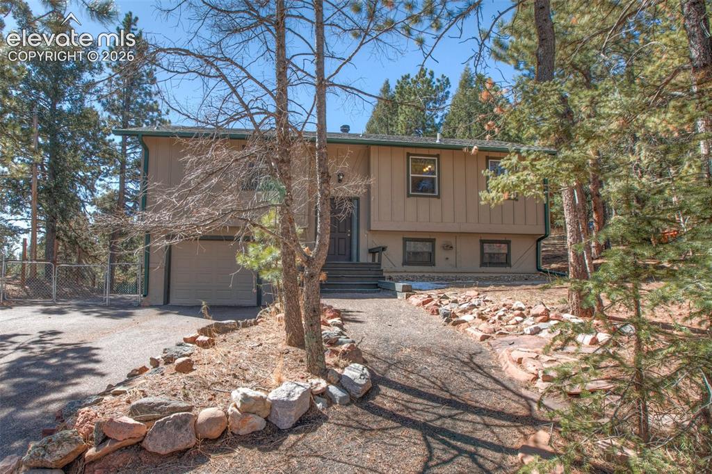 Caption: Split-level residence featuring an attached garage, front entry steps, a paved driveway, and natural