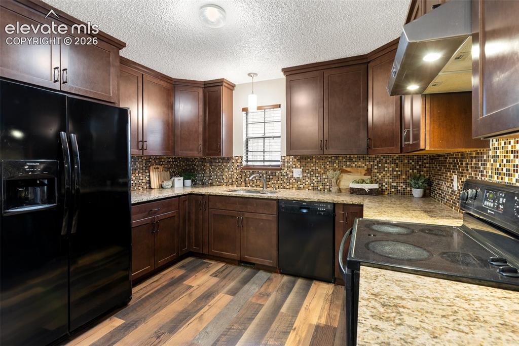 Image 11 of 41: Kitchen featuring dark wood cabinetry, a mosaic tile backsplash, granite co