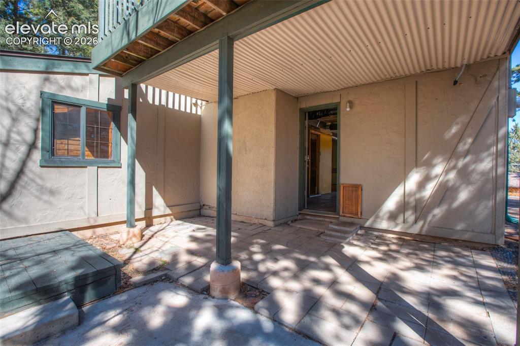 Image 33 of 41: Covered patio with corrugated metal ceiling, paver flooring, and stucco ext
