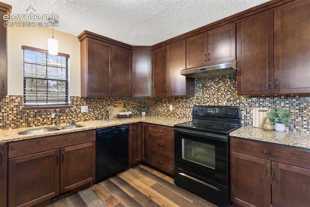 Image 8 of 41: Kitchen featuring dark wood cabinetry, a mosaic tile backsplash, granite-fi