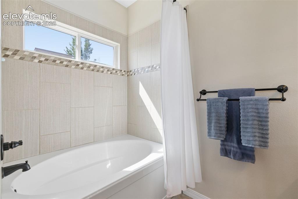 Image 25 of 48: Built-in bathtub with a white finish, tiled surround with mosaic accent, an