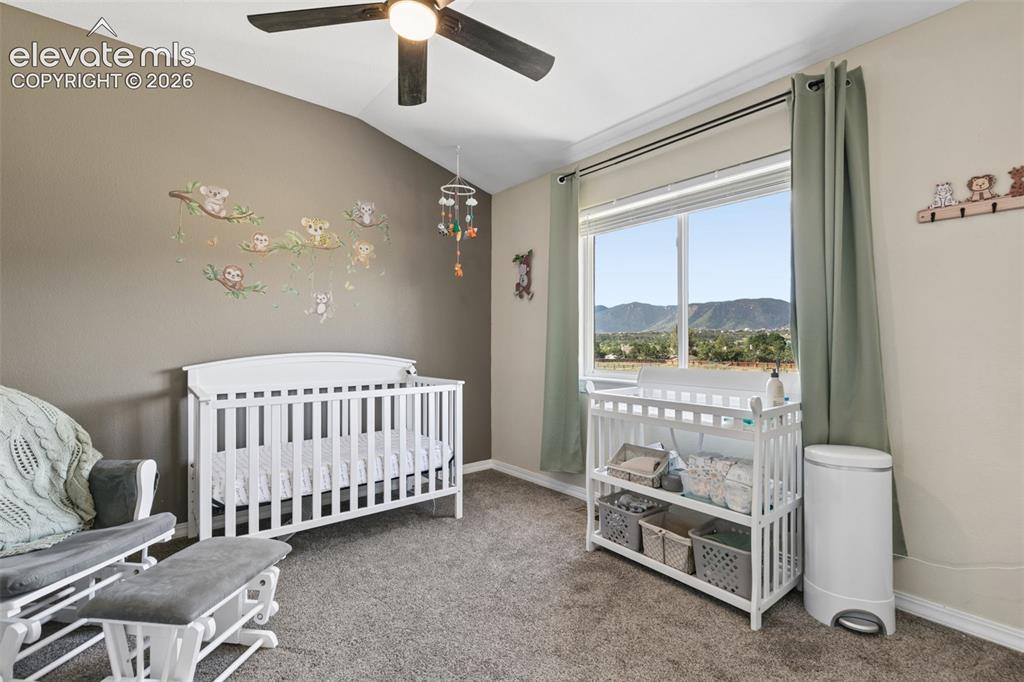 Image 26 of 48: Vaulted ceiling with a ceiling fan, carpeted flooring, and a large window w
