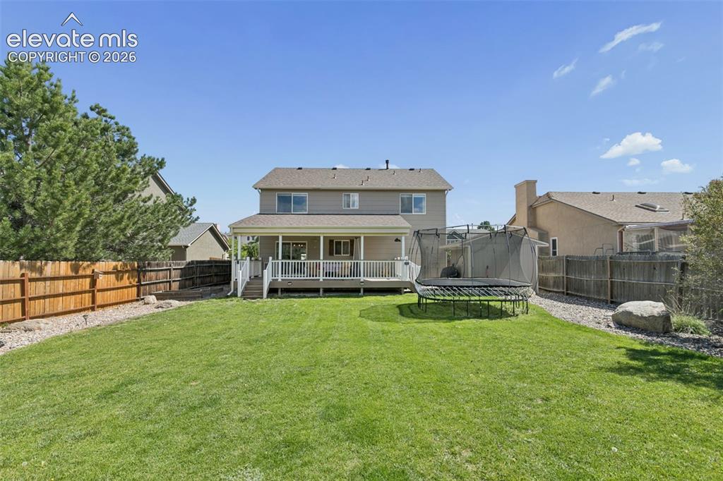 Image 39 of 48: Expansive green lawn with a covered deck, white deck railings, and a wood p