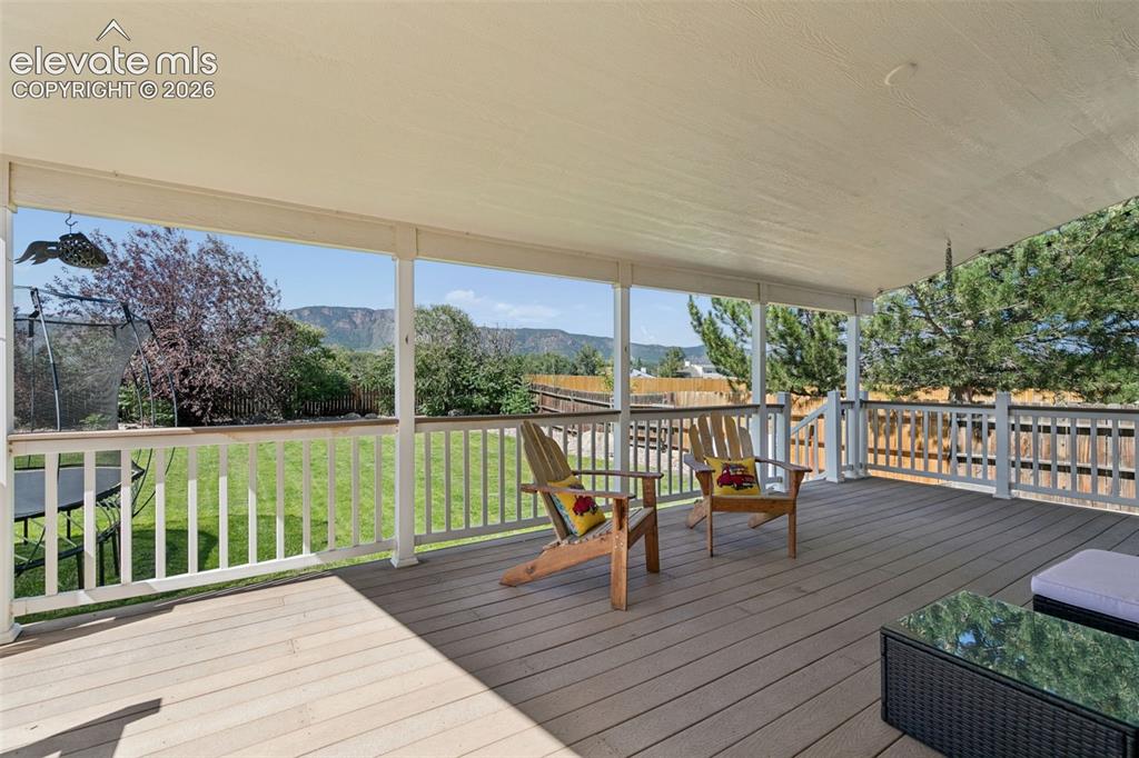 Image 6 of 48: Covered patio featuring composite decking, white railing, and a mountain ba