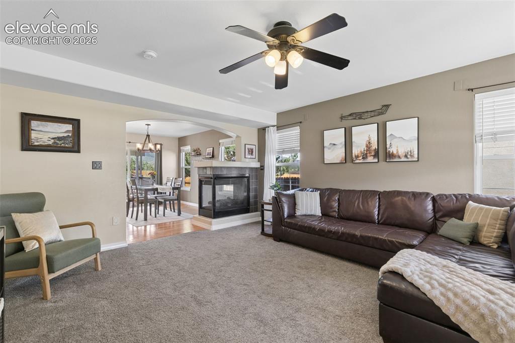 Image 7 of 48: Carpeted living area with a ceiling fan, a tiled fireplace, and a dining ro