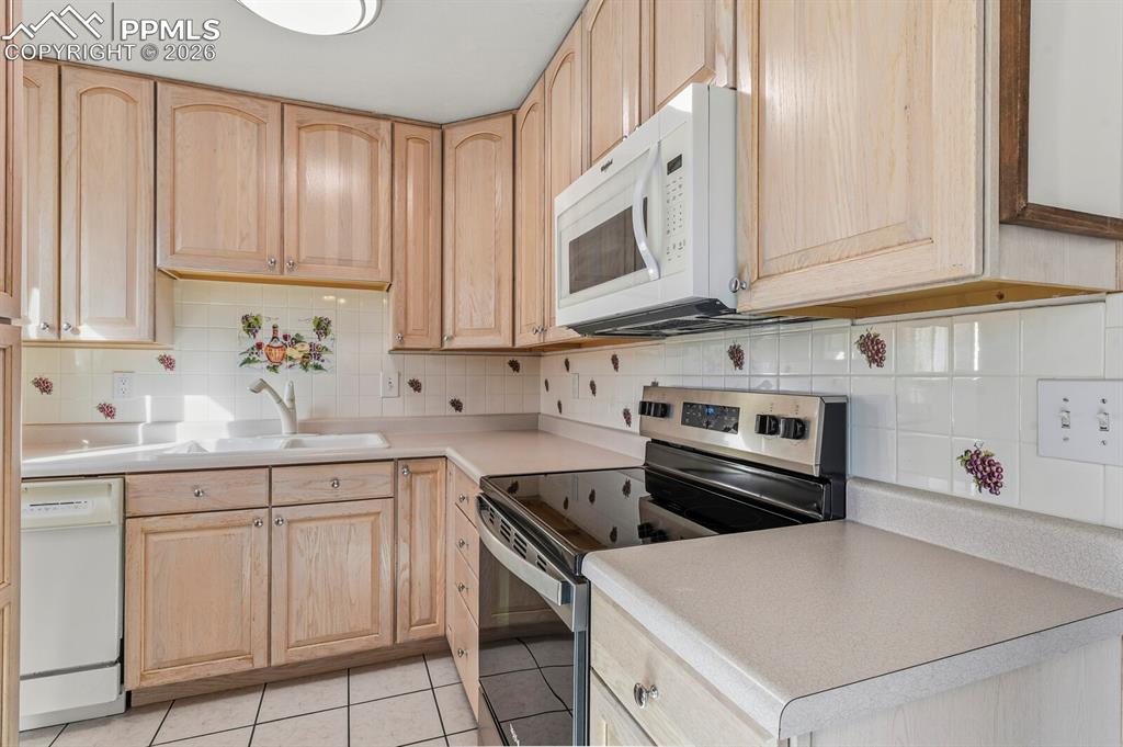 Image 12 of 49: Kitchen with light brown cabinetry, white appliances, tasteful backsplash, 