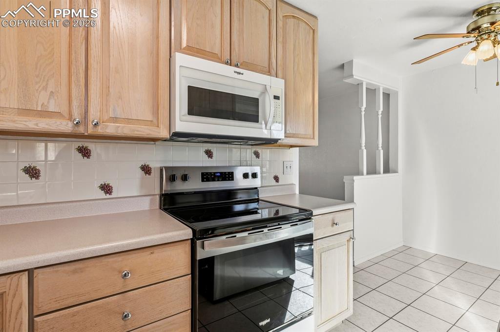 Image 14 of 49: Kitchen with stainless steel electric range, light brown cabinetry, white m