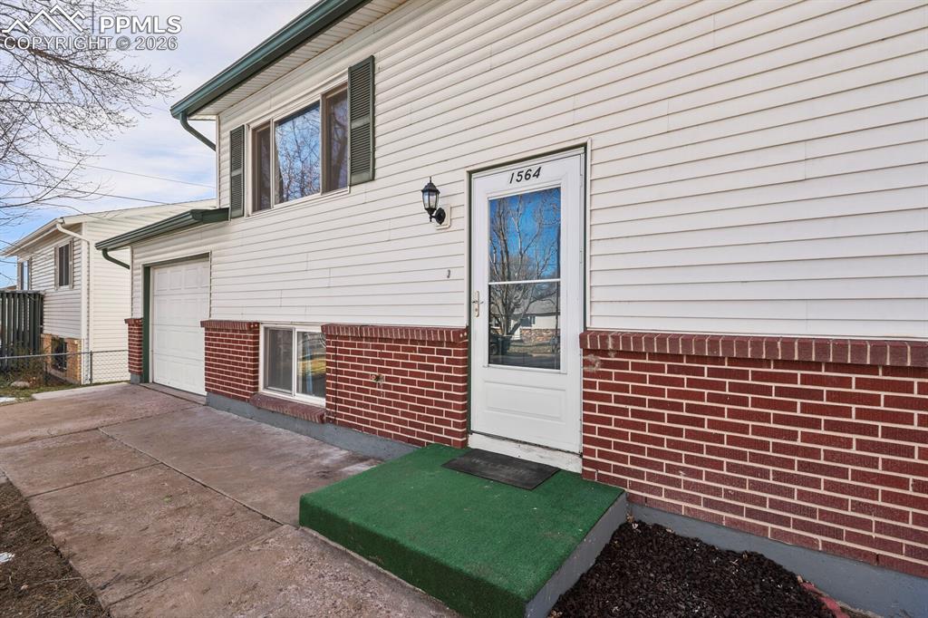 Image 3 of 49: Entrance to property with a garage, concrete driveway, and brick siding
