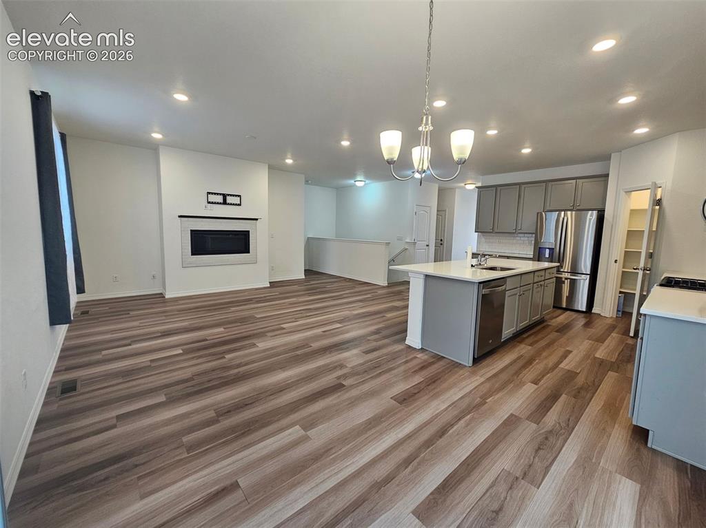 Image 12 of 25: Open-concept living area with wood-finish flooring, a contemporary fireplac