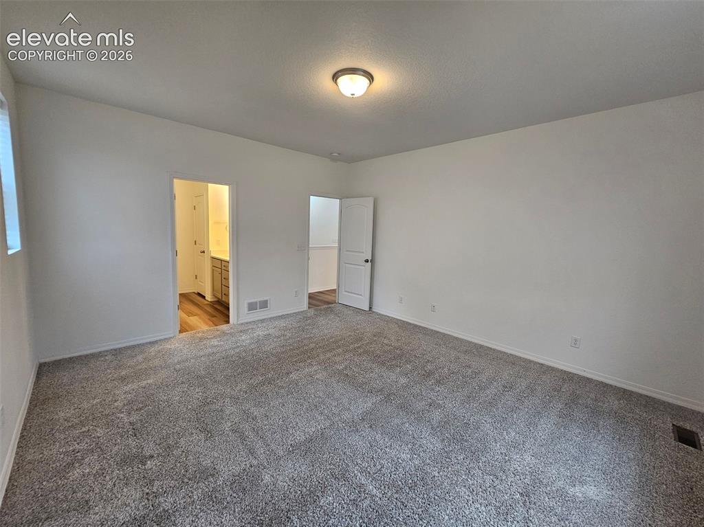 Image 13 of 25: Spacious room with plush gray carpeting, white painted walls, and a ceiling