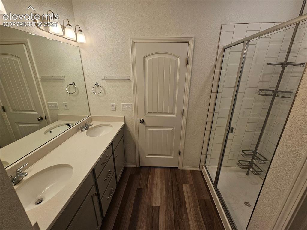 Image 16 of 25: Double vanity with integrated sinks, wood-finish flooring, and a glass-encl
