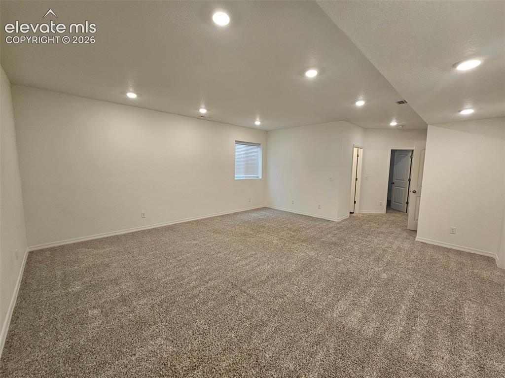Image 22 of 25: Recessed lighting illuminates this carpeted room with neutral wall tones an