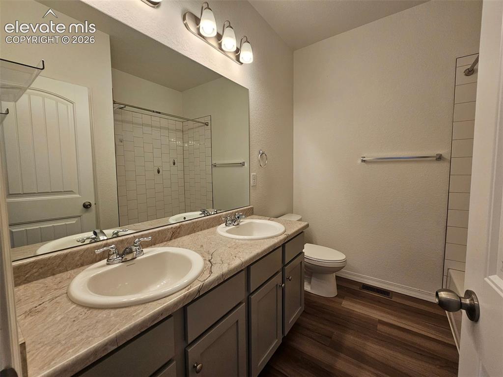 Image 5 of 25: Dual vanity with integrated sinks, wood-finish flooring, a toilet, and a sh