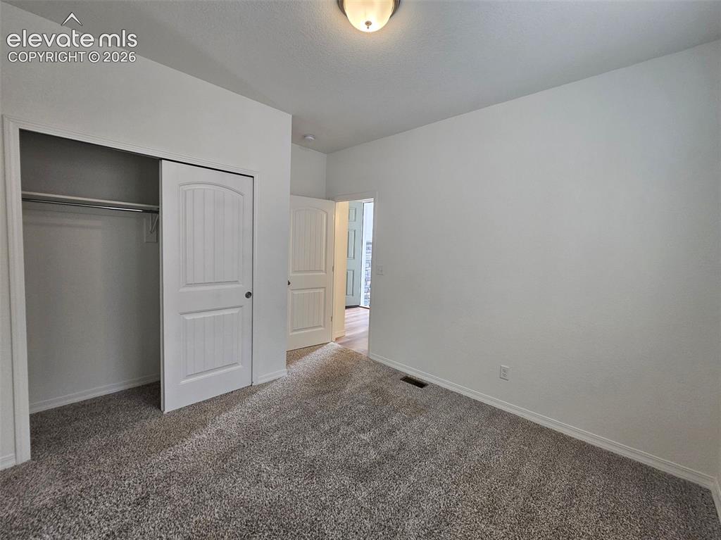 Image 7 of 25: Neutral wall paint, textured carpet flooring, bi-fold closet doors, overhea