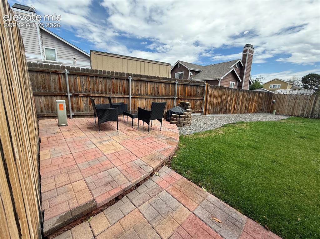 Image 12 of 15: Paver patio with a curved edge, surrounded by a wood fence, and a gravel ar