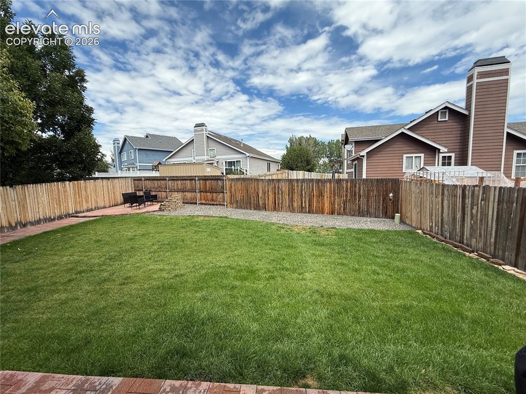 Image 14 of 15: Expansive backyard featuring a lush lawn, wood fencing, a paver patio, and