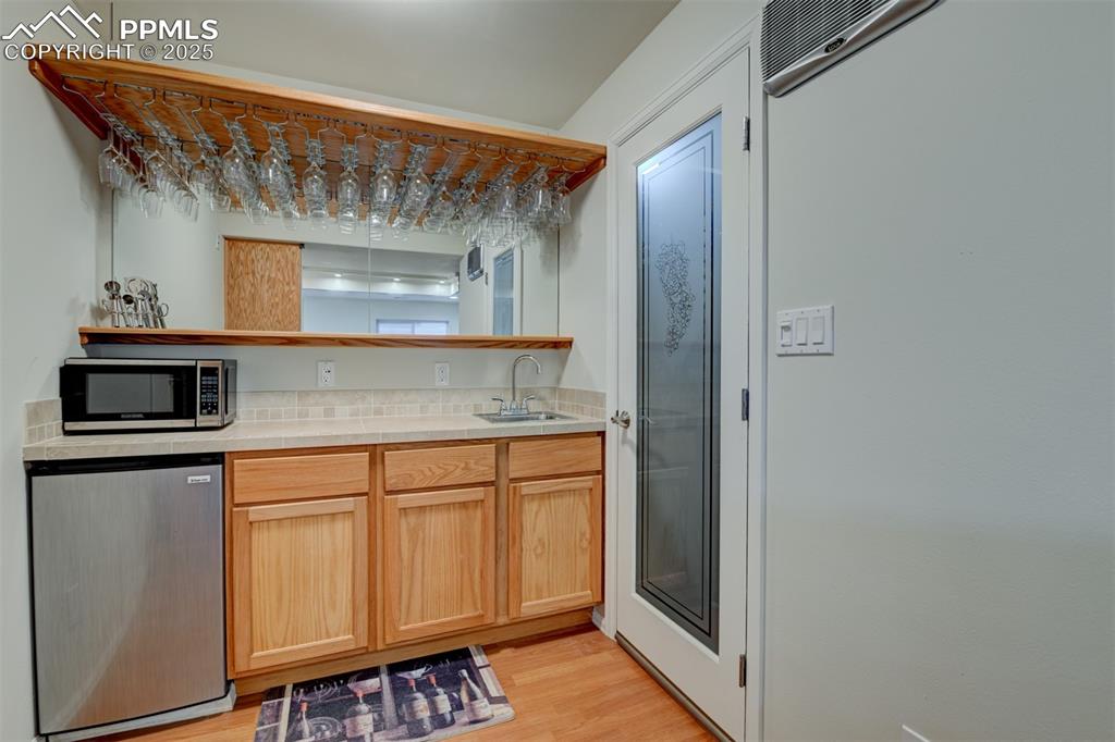 Image 36 of 47: Bar Area with Frig, Glass Rack, and Entrance to Wine Cellar.
