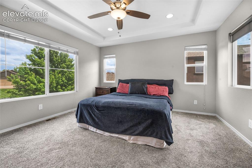 Image 14 of 34: Primary bedroom featuring a tray ceiling with a ceiling fan and recessed li