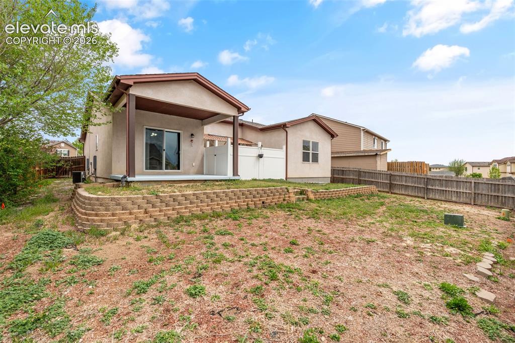 Image 12 of 20: Rear exterior featuring a covered patio, tiered decorative block retaining