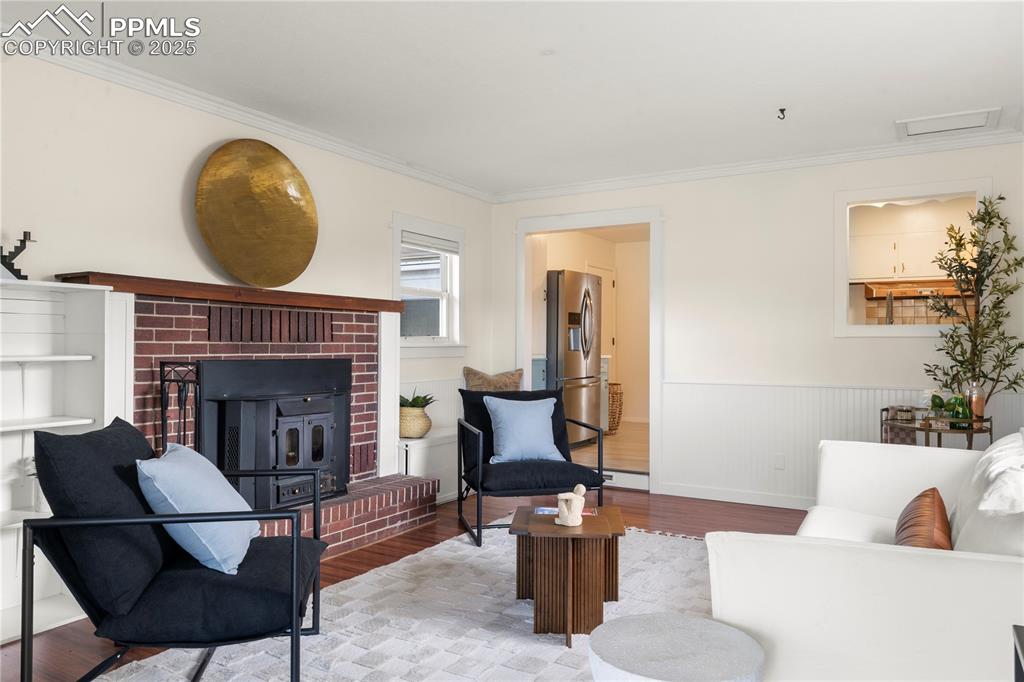 Image 11 of 30: Living area with wood finished floors, crown molding, wainscoting, and a fi