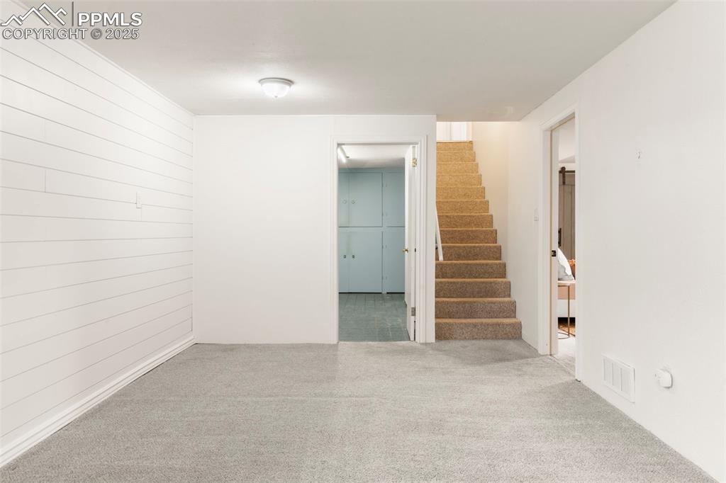 Image 17 of 30: Carpeted empty room with stairway and wood walls