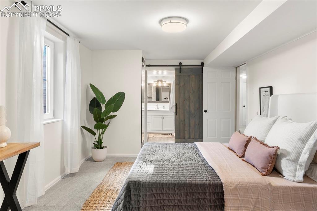 Image 19 of 30: Bedroom featuring a barn door, carpet flooring, and ensuite bath
