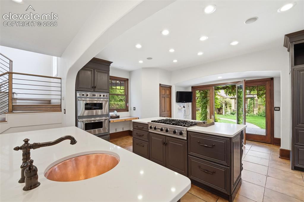 Image 11 of 50: Kitchen featuring a copper basin sink, dark wood cabinetry, a built-in doub