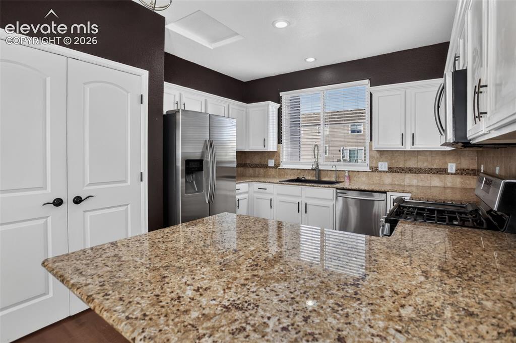 Image 14 of 46: Kitchen featuring white cabinetry, stainless steel appliances, speckled cou